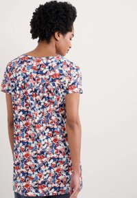 Camiseta de manga corta con estampado floral en azul, rojo y blanco, con un corte relajado y tejido suave, detalles fruncidos en la parte posterior.