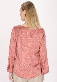 Langærmet bluse i blødt pink stof med et gyldent blomstermønster. Har en rund udskæring og en rund kant, der giver en afslappet pasform.
