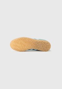 Semelle de sneaker en caoutchouc gomme, surface texturée avec des motifs circulaires et accents bleus sur le côté.