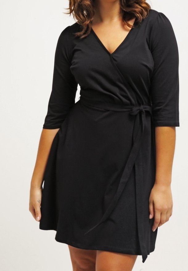 Mekko musta paketti pehmeästä kankaasta, jossa on V-pääntie, kolmivartiset hihat ja nauhavyö vyötäröllä säädettävän istuvuuden takaamiseksi.