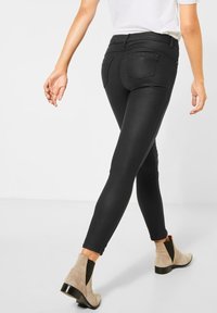 Black skinny jeans with a smooth texture and mid-rise waist, paired with beige ankle boots featuring a black elastic side panel and glossy heel.