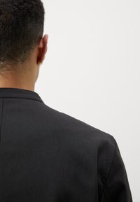 Zwarte jas met een gestructureerd ontwerp, voorzien van een nette kraag, een gladde textuur en naaddetails op de achterkant.