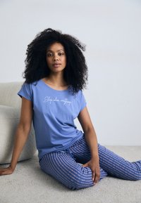 Blå kortärmad t-shirt med texten "Sömn löser allt" i vitt, parat med mönstrade blåa pyjamasbyxor med vertikala ränder.