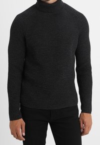 Maglione a collo alto grigio scuro a coste con maniche lunghe. Presenta un design aderente e una trama sottile. In abbinamento si vedono pantaloni neri.
