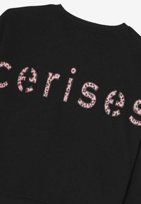 Sweat-shirt noir avec des lettres en imprimé léopard rose écrivant "cerises". Col crew classique avec bords côtelés. Texture douce et design décontracté.
