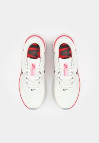 Baskets blanches de sport avec une tige texturée, accents roses sur la semelle, logo et doublure noirs, et semelles intérieures rouges avec du texte noir.