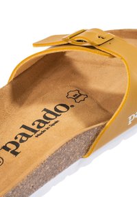 Gul läder sandal med fotbädd som har en spännsrem, korksula och en mjuk texturerad innersula. Varumärket synligt på fotbädden.