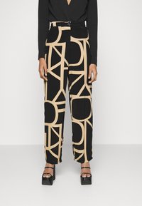 Czarne spodnie z dużymi beżowymi abstrakcyjnymi wzorami geometrycznymi, wysoki stan, szerokie nogawki oraz zapięcie na guzik w talii.