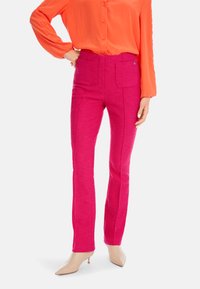 Fitted pink pants with a textured design, two front pockets, and a straight leg. Worn with an orange button-up shirt and nude heels.