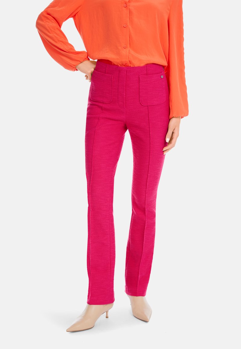 Fitted pink pants with a textured design, two front pockets, and a straight leg. Worn with an orange button-up shirt and nude heels.