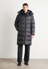 Schwarze Daunenjacke mit gestepptem Design, hohem Kragen, durchgehendem Reißverschluss und Seitentaschen. Leichtes, isoliertes Material bietet Wärme.