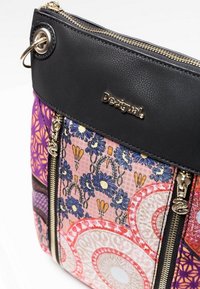Black and multicolored floral patterned Desigual bag with gold zippers and logo, featuring purple and pink decorative sections.