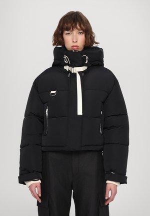 Zwarte cropped pufferjack met een hoge kraag, opvallende witte accenten, zilveren hardware en ritszakken aan elke zijde.