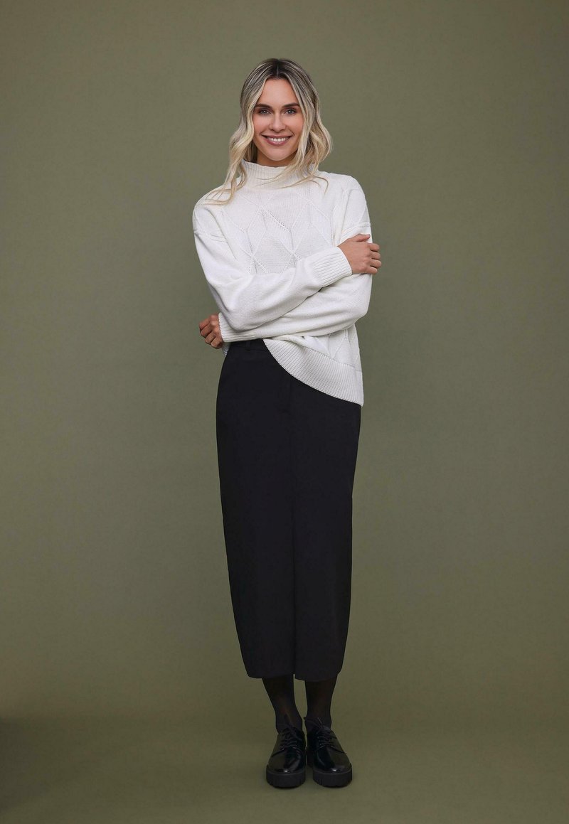 Bílý pletený rolák s texturovanými diamantovými vzory, kombinovaný s černou midi sukňou a černými platformovými botami.