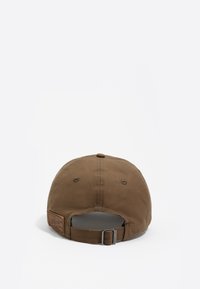 Gorra marrón de tela, con visera curva, correa ajustable en la parte trasera y un pequeño detalle de etiqueta en el costado.