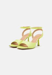 Pair of lime green high-heeled sandals with ankle straps, quilted wide front band, and pointed open toe on plain background.