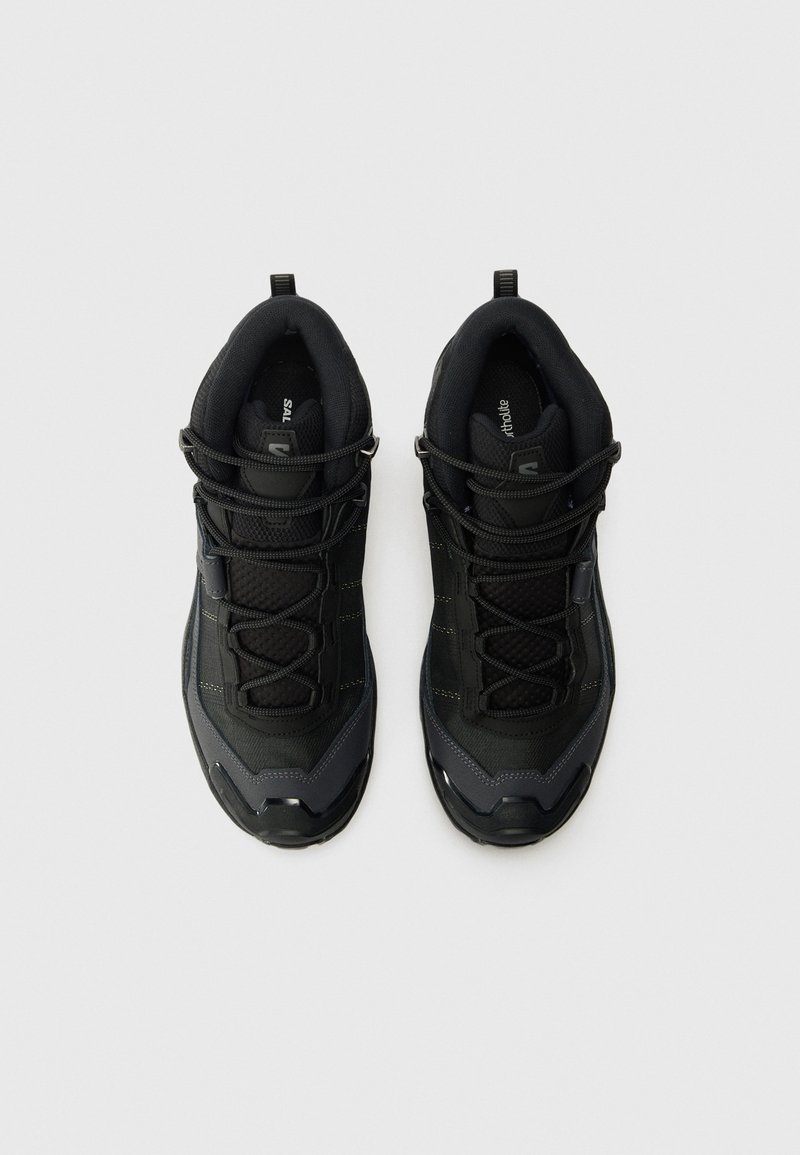 Scarpe da ginnastica nere con una tomaia in rete testurizzata, punta in gomma rinforzata e lacci elastici; caratterizzate da cuciture gialle e un collo imbottito.