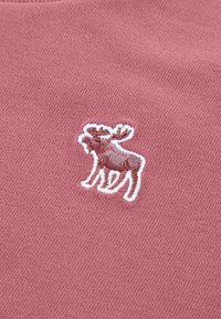 Tissu de couleur rose avec un motif détaillé de orignal brodé en brun et blanc, sur un fond lisse et texturé.