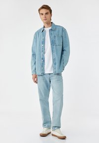 Ljusblå denimjacka med framfickor, i kombination med matchande ljusbl�å jeans och vit t-shirt. Skorna är krämfärgade med bruna sulor.