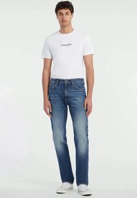 Jeans in denim blu chiaro con un fit a gamba dritta, caratterizzati da un lavaggio chiaro, sbiaditure delicate e design classico a cinque tasche. Abbinati a una t-shirt bianca con grafica.