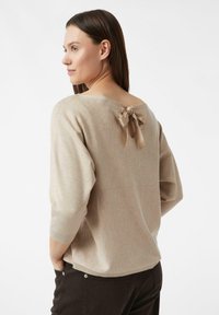 Beżowy sweter o luźnym kroju, z rękawami 3/4 i szerokim dekoltem. Z tyłu ozdobiony satynową kokardą. Miękka, dzianinowa faktura.