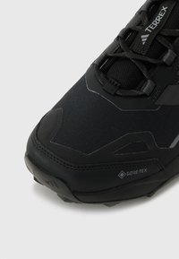 Czarne sportowe buty z chropowatej tkaniny, wzmocnionym czubkiem i oznakowaniem GORE-TEX. Ścisły system sznurowania zapewniający pewne dopasowanie.