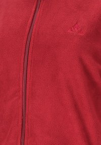 Röd fleecejacka med dragkedja, texturerad yta och en liten broderad logotyp på vänster sida.