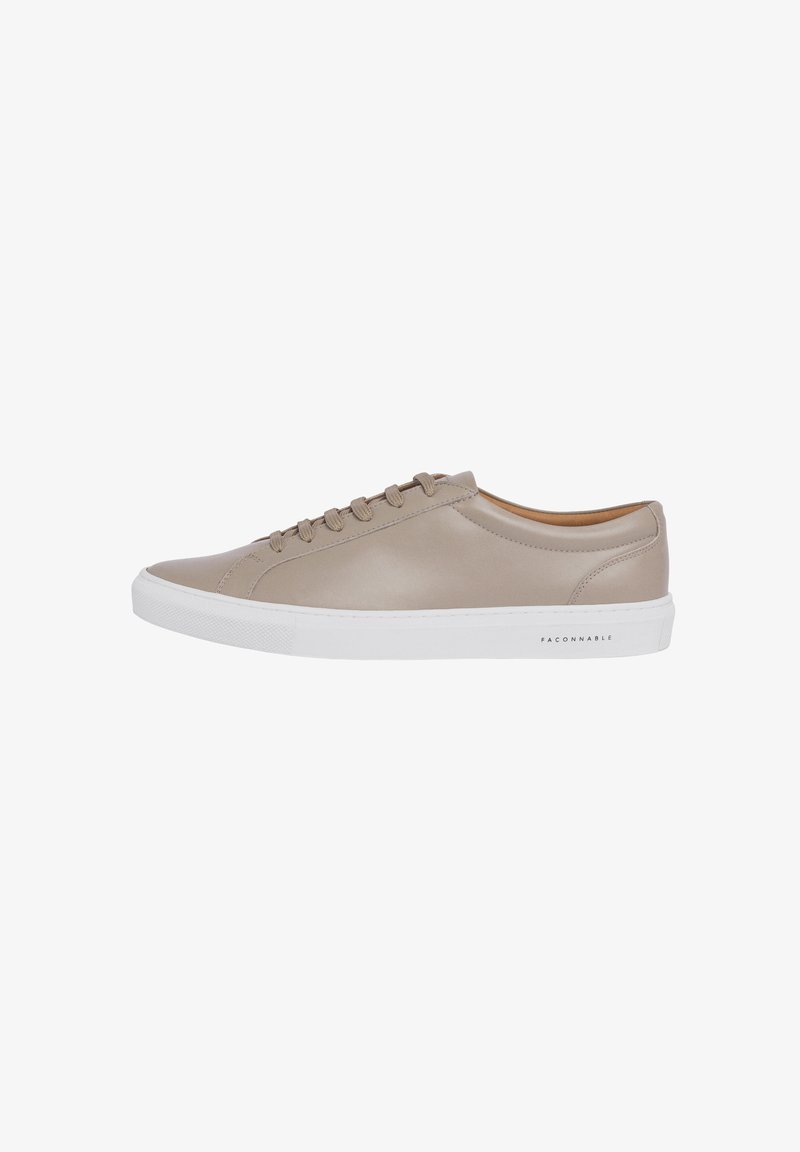 Zapatilla de cuero beige con puntera redonda, suela de goma blanca, cierre de cordones con seis ojales y un logotipo sutil en el lateral.