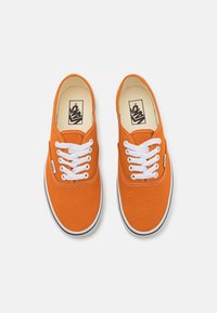 Narančaste platnene tenisice s bijelim vezicama, crnim trakama na potplatu i Vans logom na unutrašnjosti. Zaobljen vrh i glatka tekstura.