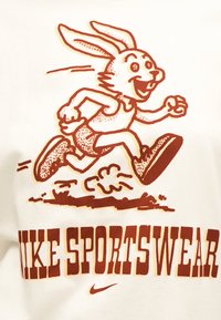 Καρτούν κουνέλι με αθλητικά ρούχα και αθλητικά παπούτσια τρέχει ενεργητικά πάνω από το έντονο κείμενο «NIKE SPORTSWEAR» και το μικρό λογότυπο του Nike swoosh.