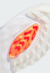 Λευκή σόλα αθλητικού παπουτσιού με έντονο πορτοκαλί λαστιχένιο στοιχείο με υφή, περιβαλλόμενη από διαφανή περιοχή και με έντονες προεξοχές για καλύτερη πρόσφυση.