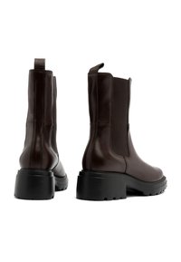 Brązowe skórzane botki za kostkę z elastycznymi panelami bocznymi, okrągłym noskiem i masywną czarną podeszwą. Wyposażone w uchwyt z tyłu dla łatwego zakładania.