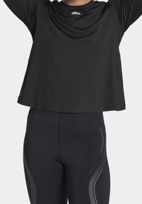 Svart atletisk långärmad topp med rund halsringning, lätt textur; kombinerad med figurnära svarta leggings med grå sidodetaljer.