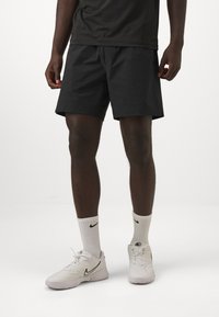 Pantalones cortos deportivos negros con un corte relajado, hechos de tejido ligero. Combinados con zapatillas Nike blancas y calcetines a juego para crear contraste.