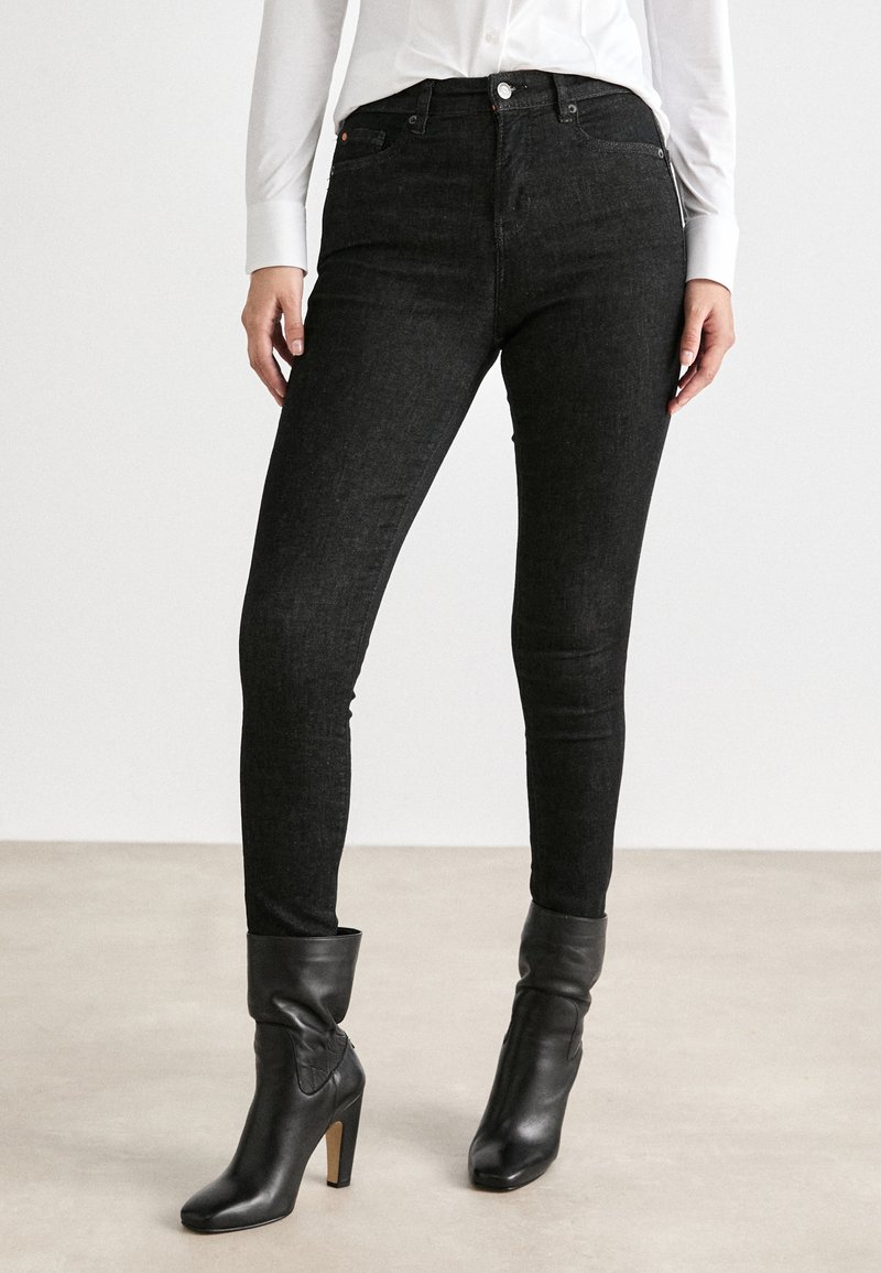 Černé skinny džíny vyrobené z pružného denimu, s vysokým pasem a klasickým designem pěti kapes. V kombinaci s upnutými černými kotníkovými botami.