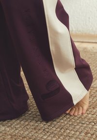 Burgundske pajkice s kremnimi stranskimi vložki, z izbočeno besedilo "BY TED BAKER" in stilizirano številko, mehka tkanina in sproščen kroj.