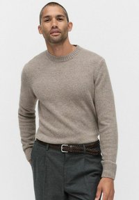 Beżowy sweter z okrągłym dekoltem i długimi rękawami, wykonany z mi�ękkiego, teksturowanego materiału. Zestawiony z szarymi spodniami i plecionym brązowym skórzanym paskiem.