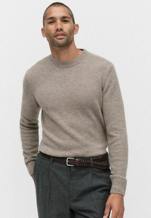 Beige rundringad tröja med långa ärmar, tillverkad av mjukt texturerat material. Kombineras med grå byxor och ett flätat brunt läderbälte.