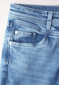 Jeans de denim azul claro con una textura suave, que cuentan con un pequeño bolsillo frontal, remaches de metal y costuras en contraste a lo largo de la cinturilla.
