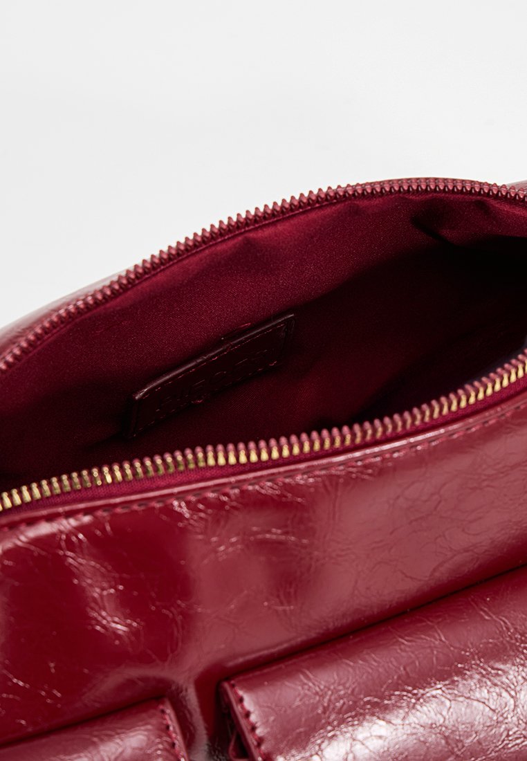 Rote Kunstleder-Handtasche mit einem Reißverschluss. Innenfutter aus passendem Satin mit einem Etikett und glatter Textur.