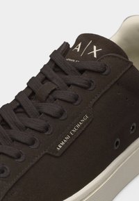 Baskets Armani Exchange de couleur marron foncé avec des lacets noirs, une semelle blanche, et le logo A|X sur la langue et le panneau latéral.