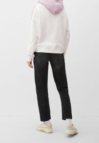 Felpa bianca con cappuccio rosa, abbinata a jeans neri a gamba dritta e sneakers beige. L'outfit presenta una vestibilità rilassata e texture morbide.