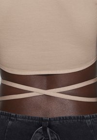 Top ajustado beige con un acabado texturizado, con tirantes cruzados en la parte posterior, acompañado de una tela gris oscuro y texturizada en la parte inferior.