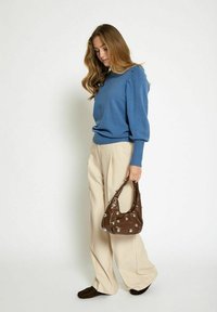 Pull bleu avec manches bouffantes, pantalon large crème et sac à main marron avec des accents métalliques. Tissu lisse et coupe décontractée.
