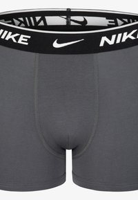 Sivi bombažni raztegljivi bokserici z črnim elastičnim pasom z logotipom "NIKE" in belim detajlom Swoosh. Gladka tekstura in tesen fit.