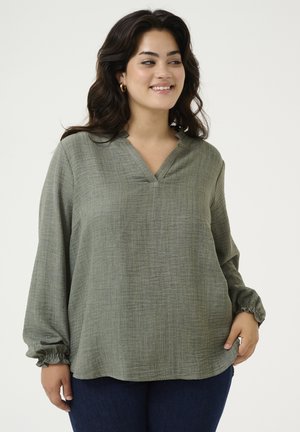 Blusa larga de manga larga verde, texturada, con escote en V y puños fruncidos, presenta un corte holgado y un sutil patrón horizontal.