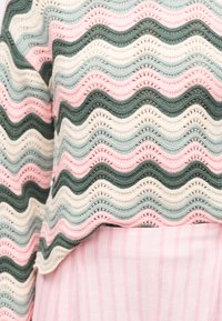 Πλεκτό πουλόβερ με κυματιστές ρίγες σε ροζ, πράσινο, κρεμ και ανοιχτό μπλε πάνω από ροζ και λευκή ριγέ φούστα ή παντελόνι.