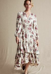 Kwiatowa sukienka maxi w kremowym kolorze z bordowymi i niebieskimi kwiatami, z warstwowym falbanowym dołem, długimi rękawami i dekoltem w serek. Miękka, lekko opadająca tkanina.