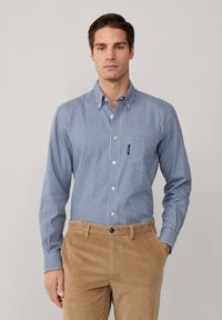 Camisa de cuadros azul y blanca con botones y largas mangas, con un bolsillo, combinada con pantalones de pana marrón. Textura suave, ajuste estructurado.