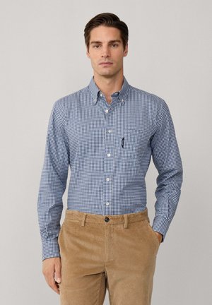 Camisa de cuadros azul y blanca con botones y largas mangas, con un bolsillo, combinada con pantalones de pana marrón. Textura suave, ajuste estructurado.